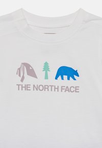 Λευκό μπλουζάκι με γραφικό γκρι βουνού, πράσινου δέντρου και μπλε αρκούδας. "THE NORTH FACE" είναι τυπωμένο σε γκρι κάτω από τα γραφικά.