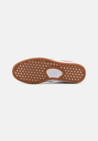 Vans fottøy med gummisåle, med et diamantmønster for grep. Hovedsakelig brun med hvite detaljer og en logo.