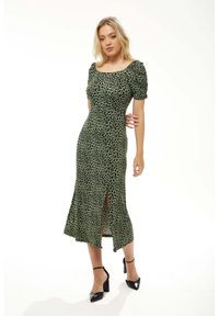 Green leopard print dress with short puff sleeves, fitted silhouette, mid-length hemline, and side slit; smooth texture, paired with black heels.