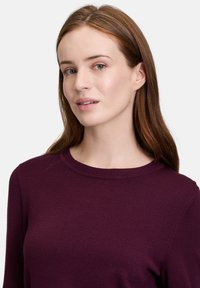 Maglione in maglia viola con collo a giro e maniche lunghe, caratterizzato da una texture liscia e dettagli a coste sottili sul colletto.
