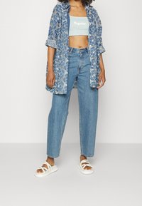 Jasnoniebieska, kwiecista koszula oversize, jasnoniebieski krótki top, niebieskie spodnie z wysokim stanem i białe sandały na ramiączkach.