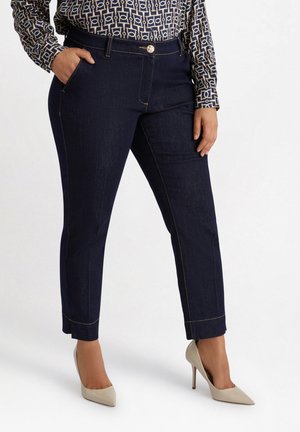 Navy blue denim trousers featuring a fitted design, pocket at the side, and gold stitching with a cropped hem. Paired with beige high heels.