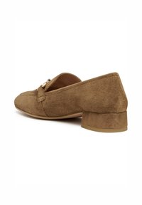 Mocasín de ante marrón con un tacón bajo, que presenta un acento decorativo de hardware en tono dorado en la parte delantera y un diseño de punta redondeada.