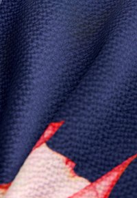 Zbliżenie na teksturowaną granatową tkaninę z czerwono-białym wzorem gwiazd, ukazujące zagięcia, szczegóły splotu i kontrast kolorów.