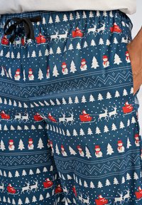 Blauwe pyjamabroek met een feestelijk patroon van sneeuwmannen, kerstbomen, rendieren en sleeën in rood en wit. Elastische tailleband met trekkoord.