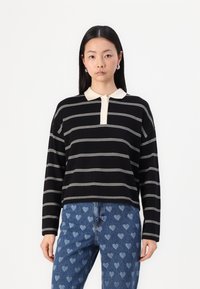 Black and white striped long-sleeve polo shirt with a beige collar and three buttons, paired with faded blue jeans featuring heart patterns.