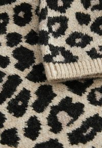 Tissu en tricot à imprimé léopard beige avec des taches noires. Texture douce avec un bord côtelé. La vue en gros plan met en évidence le détail du motif et des fibres.