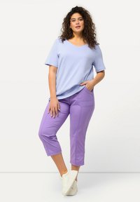 Haut bleu clair à manches courtes associé à un pantalon lavande mi-mollet. Le pantalon est doté de poches et est fabriqué dans un matériau lisse et extensible. Baskets blanches.