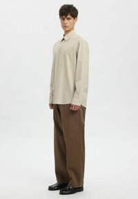 Hele beež ruuduline särk nööpidega varrukakaelusega, kombineeritud lahtiste pruuni värvi pükstega ja mustade nahast kingadega. Sile kangapind.