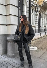 Melna pārspīlēta vilnas jaka, melni ādas bikses un masīvas melnas zābaki. Maza melna izšūta rokassoma ar sudraba piederumiem un logotipu.