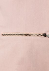 Vaaleanpunainen kangas, jossa on vinoa nauha- ja pinta, ja metallinen vetoketju, joka kulkee vaakasuorasti keskellä.