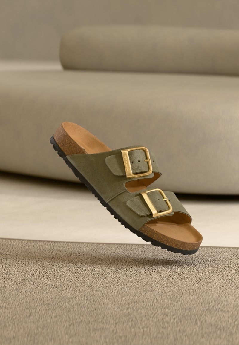 Sandale mule en daim vert olive avec deux boucles dorées, semelle intérieure en liège marron et semelle extérieure en caoutchouc noir texturé.