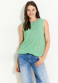 Grön- och vitrandig ärmlös topp med lös passform, l ättviktsmaterial och rund halsringning, i kombination med ljusblå jeans.