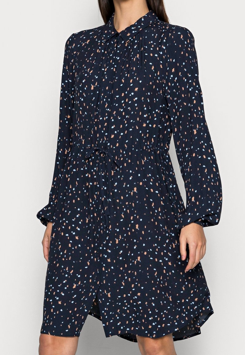Abito lungo a maniche lunghe blu navy con colletto, chiusura a bottoni frontale, cintura in vita e macchie astratte sparse in azzurro chiaro e beige.
