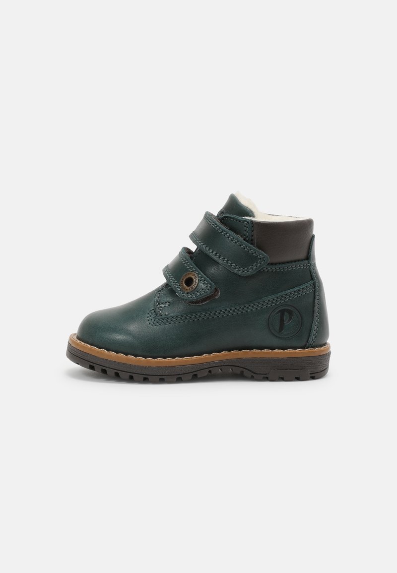 Botas de tobillo de cuero verde con dos correas de Velcro, un acento de cuero marrón en la parte superior y una suela de goma texturizada marrón.
