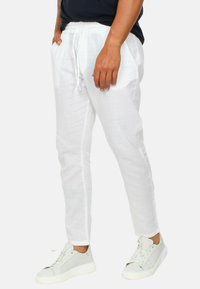 Pantaloni di lino bianchi con una vestibilità dritta, vita con coulisse e tasche laterali, abbinati a sneaker grigio chiaro a piedi nudi.