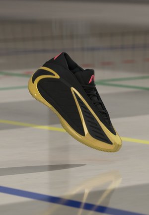 Pantof sport negru plutitor cu accente aurii și logo roșu, prezentat în aer deasupra unui teren cu linii colorate.