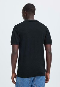 Polo noir à manches courtes avec un col classique, une texture lisse et une coupe régulière, associé à un short en denim bleu clair.