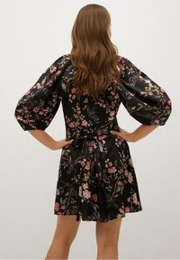 Vestido negro con flores y mangas abullonadas, ceñido a la cintura con un lazo. Presenta patrones florales en tonos rosa y verde sobre un fondo oscuro.