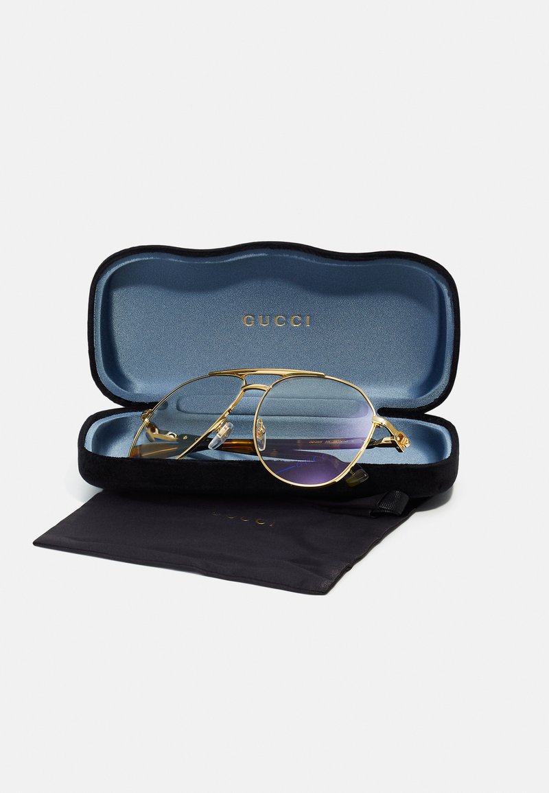 Goldfarbene Pilotenbrille mit einem lila Verlaufsglas, untergebracht in einem schwarzen und blauen Hartschalenetui. Enthält ein schwarzes Mikrofaserbeutel.