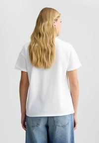 T-shirt en coton blanc à manches courtes, coupe ample et encolure ronde, associé à un jean en denim bleu clair taille haute.
