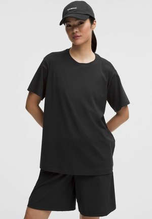 Czarny bawełniany T-shirt o luźnym kroju i krótkich rękawach, zestawiony z czarnymi szortami. Całość dopełnia czarna czapka z białym logo.