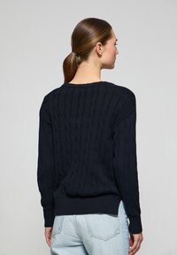 Mörkblå kabelstickad tröja med rundad halsringning och ribbad manschetter. Har ett strukturerat mönster och en något lös passform.