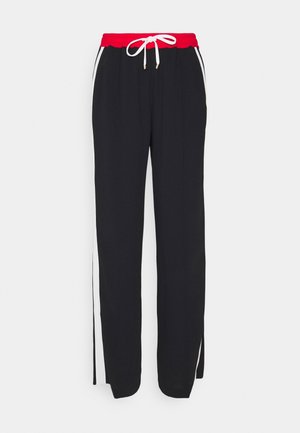 Schwarze Jogginghose mit rotem, elastischem Bund, weißem Kordelzug und weißen Seitenstreifen, flach auf einem weißen Hintergrund liegend.