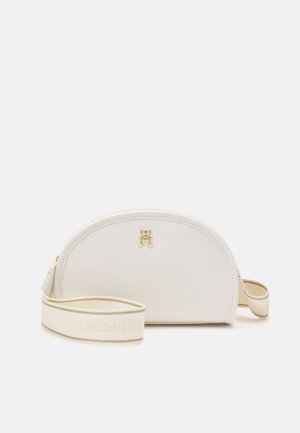 Petit sac bandoulière blanc en forme de demi-lune avec logo doré "TH" et large sangle crème avec inscription discrète "HILFIGER".