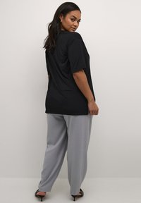 T-shirt noir surdimensionné à manches courtes, associé à un pantalon large gris clair. Tissu lisse, coupe décontractée et sans motifs visibles.
