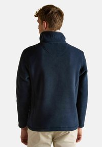 Námořnický fleecový pulovr s vysokým límcem a vyšitým logem na zadní straně. Měkká textura, rovný střih a žádné viditelné zapínání.