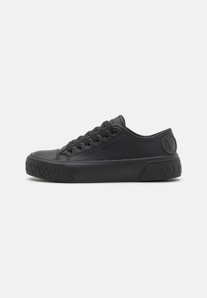 Zapatilla negra de corte bajo con cierre de cordones, suela texturizada y logo "V" en relieve en el talón sobre un fondo claro y sencillo.