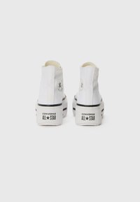 White high-top sneakers with a thick platform sole. Features circular black logo accents, and contrasting black stripes along the base.
