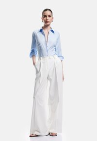 Light blue button-up shirt with rolled sleeves, paired with high-waisted white wide-leg trousers. Textured fabric, minimalistic design.