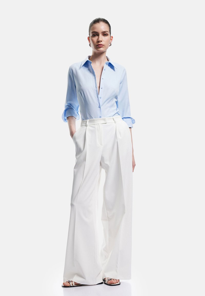 Light blue button-up shirt with rolled sleeves, paired with high-waisted white wide-leg trousers. Textured fabric, minimalistic design.