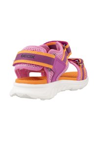 Sandalia rosa y morada con parte superior de malla, plantilla naranja, suela de goma blanca, correas ajustables y detalles de marca en el talón.