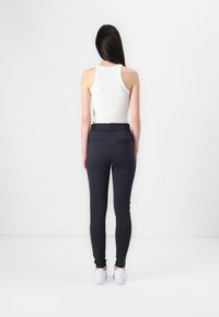 Sorte tapered bukser med elastisk liv og to baklommer, sammen med en hvit ermeløs topp. Glatt stoff og tettsittende design.