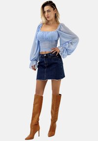 Himmelblausa, dehnbare Bluse mit Puffärmeln und quadratischem Ausschnitt, kombiniert mit einem dunklen Jeans-Minirock und kniehohen braunen Stiefeln mit Absatz.