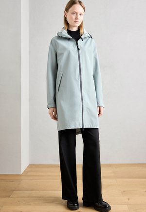 Light blue waterproof jacket with a hood, front zip, and side pockets. Paired with black wide-leg pants and chunky black shoes.