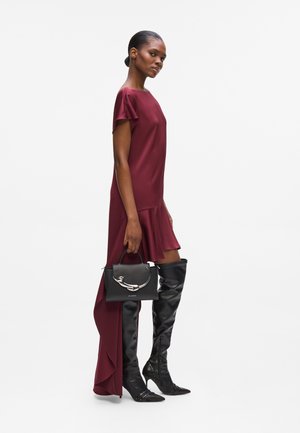 Vestido burdeos con mangas cortas y dobladillo asimétrico, combinado con botas de cuero negras hasta la rodilla y un bolso negro con detalles plateados.