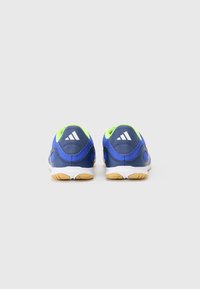 Zapatillas deportivas azules con parte superior de malla texturizada, acentos amarillos y suelas blancas. Presentan una forma redondeada y un logotipo de marca visible en el talón.