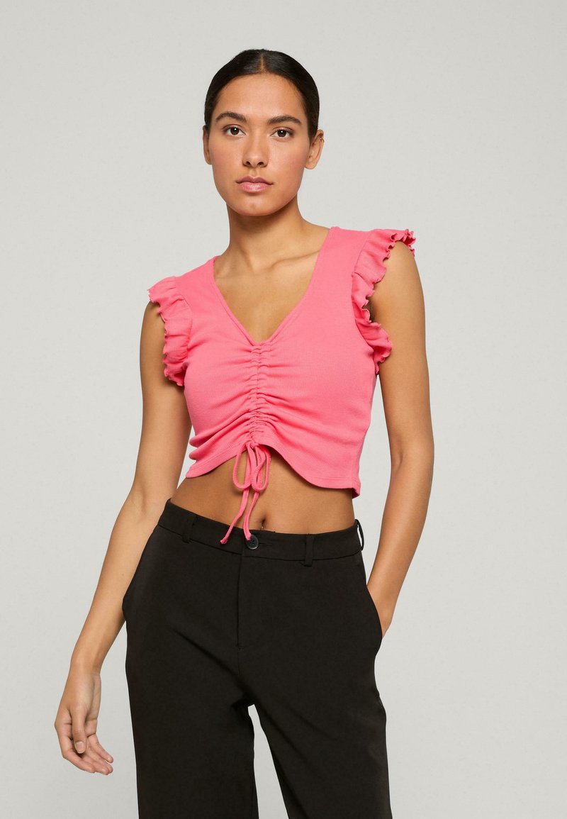 Top corto rosa con maniche a volant, caratterizzato da un fondo a V e un lacciolo anteriore. Abbinato a pantaloni neri a vita alta. Texture liscia.
