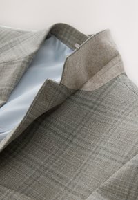 Blazer in lana grigio chiaro con motivo a quadri, caratterizzato da un morbido colletto beige e una fodera interna liscia blu. Design pulito e strutturato.