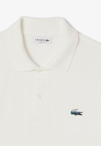 Witte polo shirt van textuurstof, met twee knopen en een klein geborduurd groen en rood krokodillogo op de linkerborst. Klassieke pasvorm.