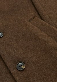 Ruda vilnos mišinio medžiaga su lygiu paviršiumi, turinti dvigubą mygtuko užsegimą ir kišenę su atvartu.