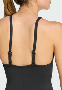 Černé plavky s nastavitelnými, úzkými ramínky a hladkou, matnou texturou. Pohled zezadu, ukazující minimalistický design.