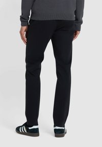 Zwarte broek met een rechte snit, gemaakt van een gladde stof. Draag ze met donkere sneakers met witte strepen en accenten.