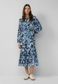 Abito camicia floreale in blu chiaro e nero, con maniche lunghe, chiusura frontale con bottoni, orlo a strati e tessuto testurizzato. Abbinato a sneaker bianche.