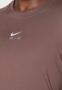 Brun sporttröja med rundad halsringning, gjord av ett slätt material. Har en vit Nike-logotyp och texten 'AIR' på framsidan.