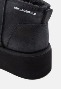 Botín negro de plataforma hecho de tejido suave con un forro blando. Cuenta con una forma redondeada, suela plana y el logo "KARL LAGERFELD" en el lateral.